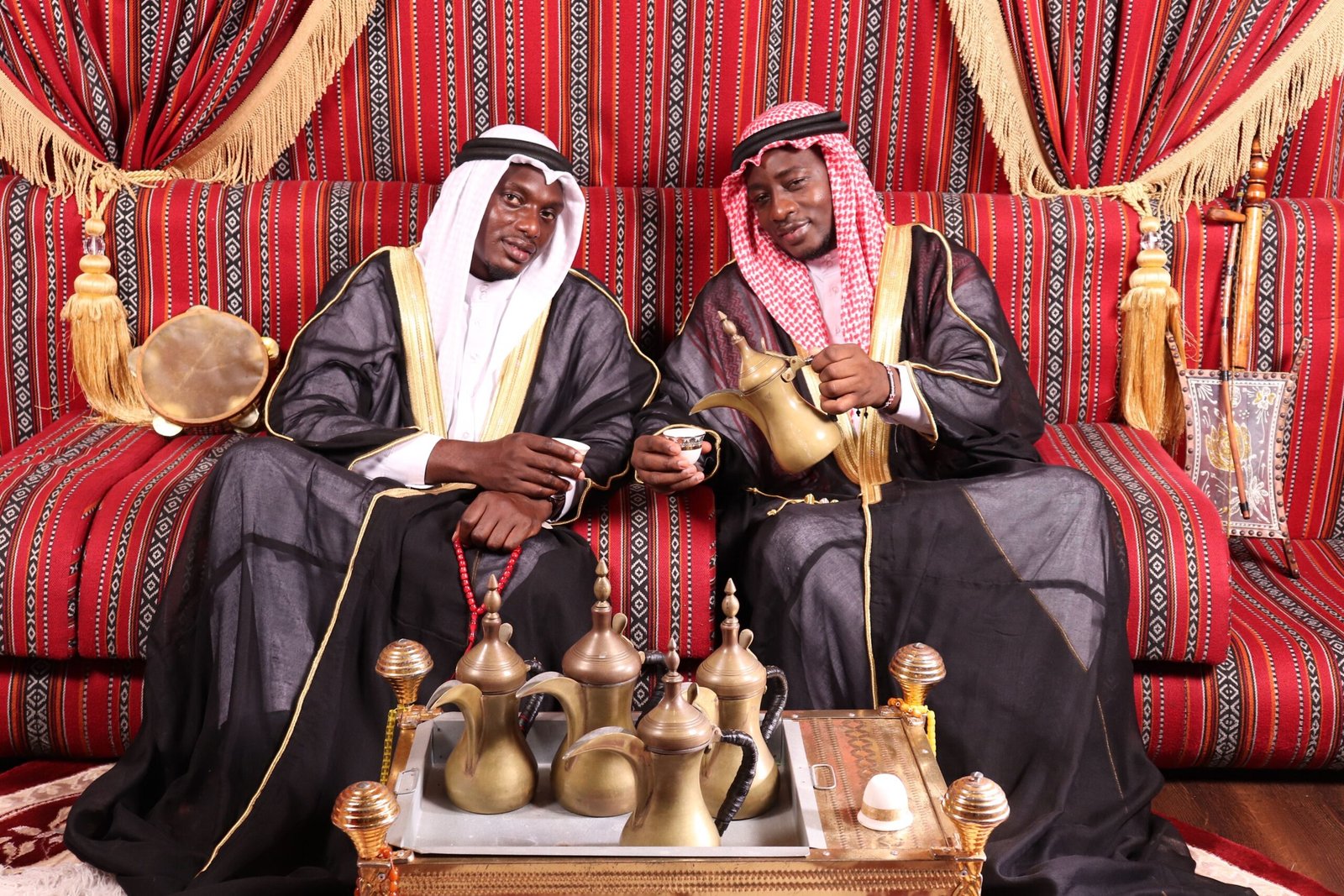 Two men in traditional attire enjoy a tea ceremony indoors, reflecting cultural heritage.