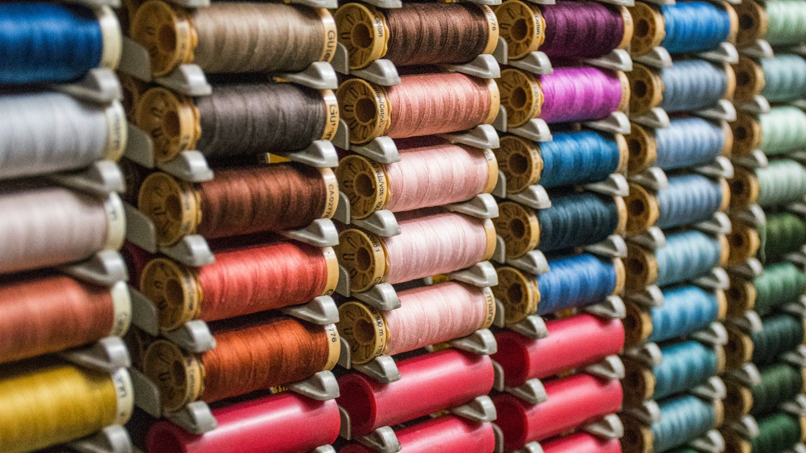 Colourful thread spools on a mill shelf, the yarn stage where thobe fabric hand feel and count are set