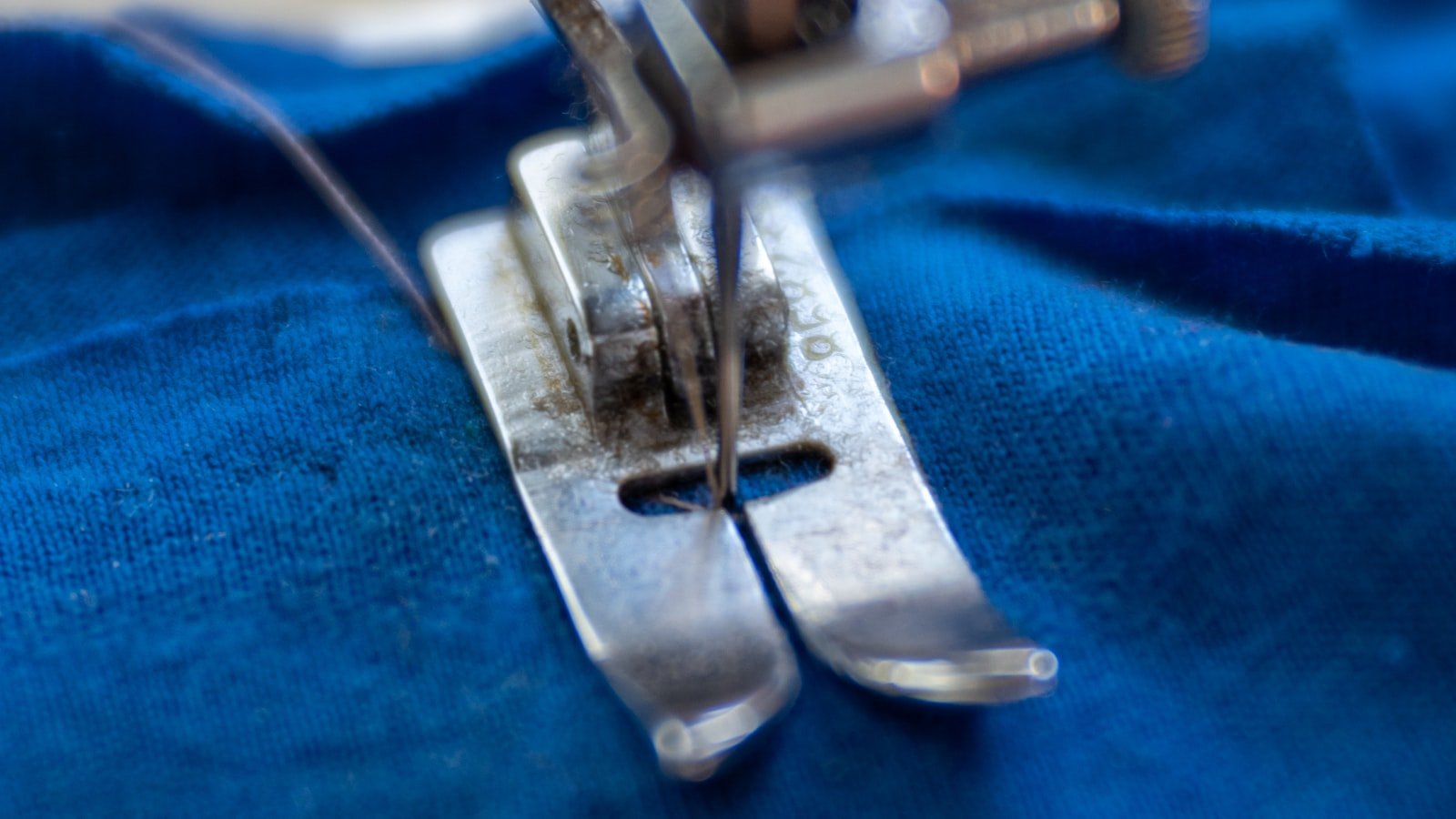 A sewing machine stitching a blue textile panel, the garment stage where thobe fabric weight and drape are tested in production
