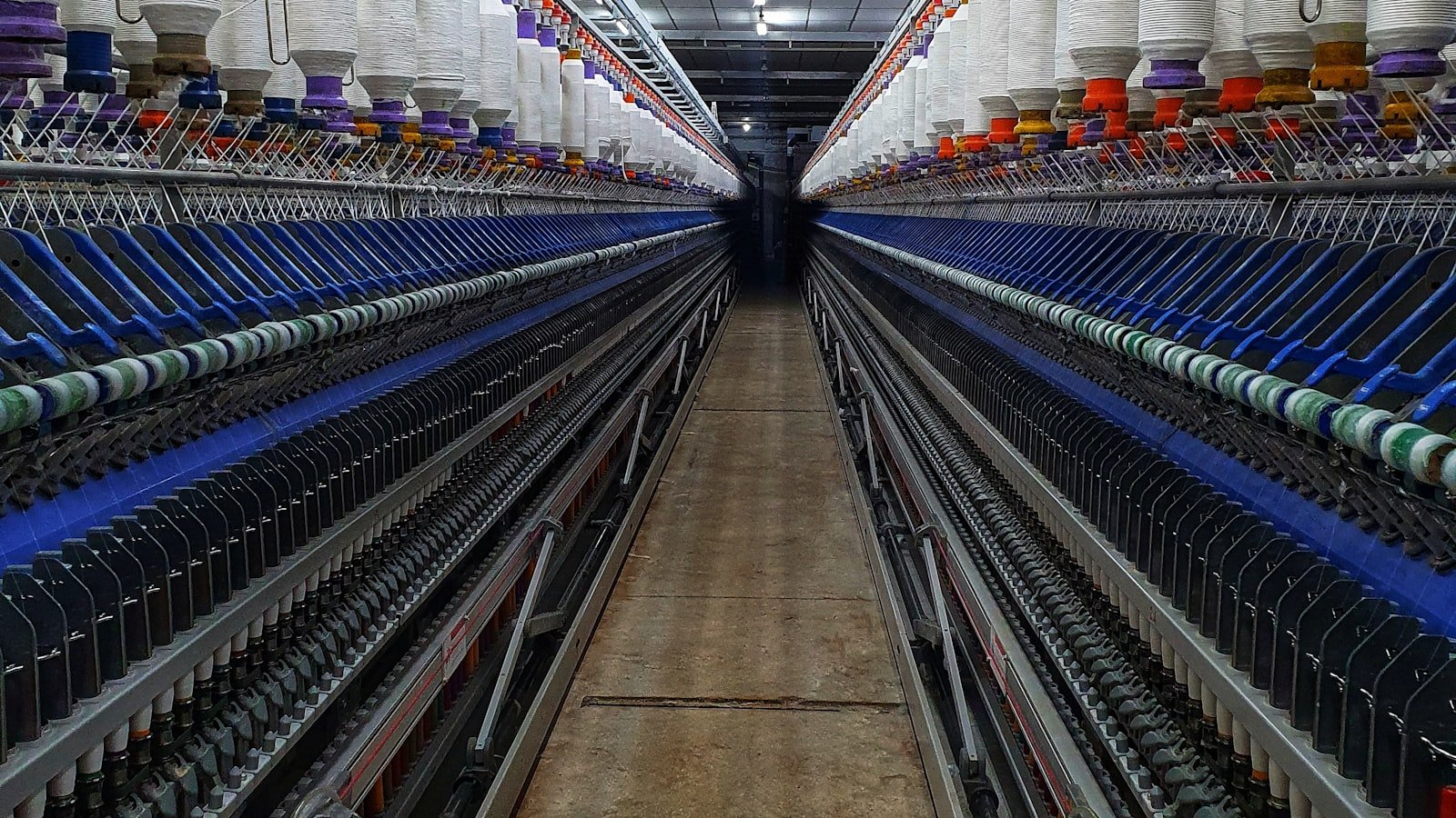 Rows of textile machinery and yarn spools inside a weaving mill, evidence of the production scale a genuine thobe fabric factory can show a buyer