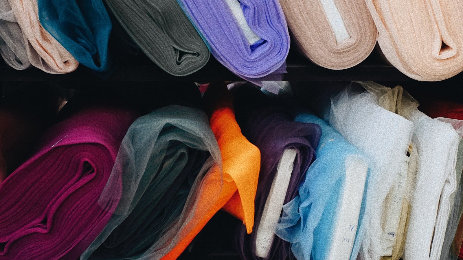 Folded thobe fabric in a range of colours on a mill shelf, showing the shade range available in certified and recycled constructions