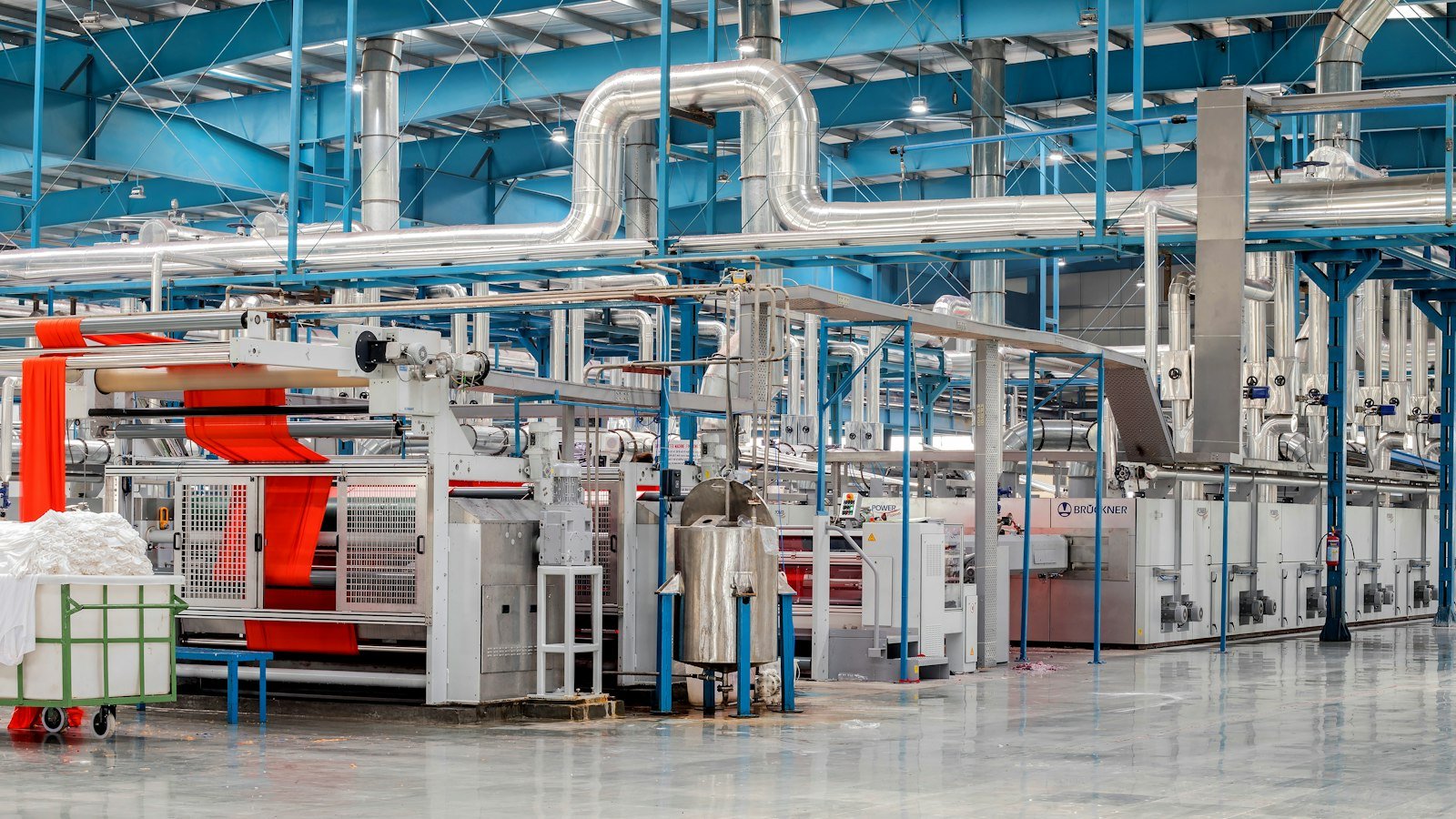 Industrial textile mill floor with rows of machinery and overhead service pipework